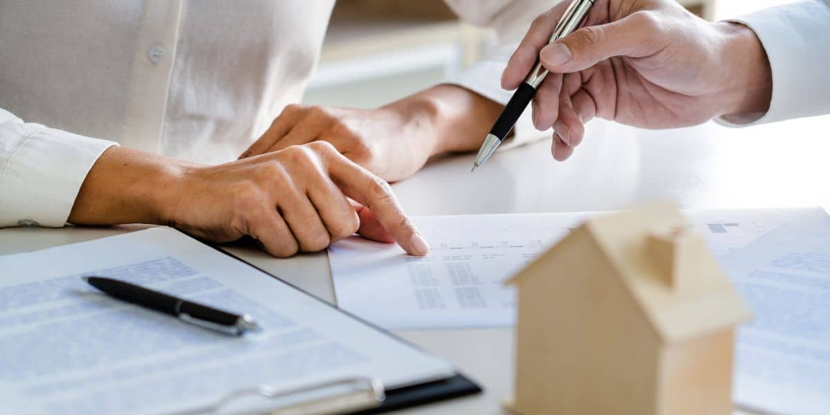 Close-up of two people discussing a real estate title with one pointing and the other holding a pen, with a model house in the foreground.